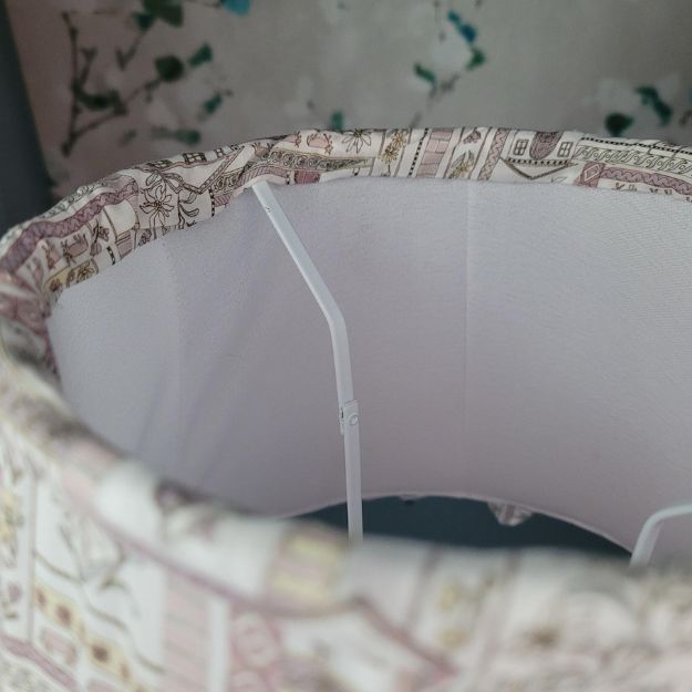 Tapered hand-sewn fabric French drum lampshade featuring alpine flowers and animals in a whimsical design. Finished with ruffle trim for a charming touch, adding a unique and cosy element to any table lamp. Crafted with Liberty London fabric.