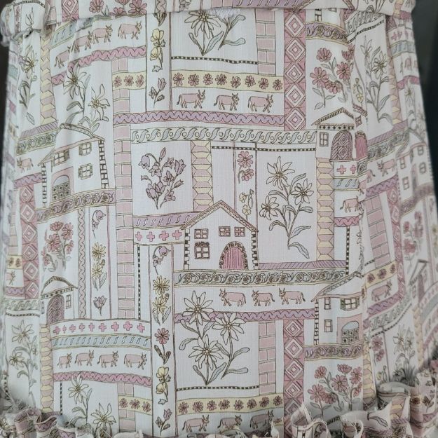 Tapered hand-sewn fabric French drum lampshade featuring alpine flowers and animals in a whimsical design. Finished with ruffle trim for a charming touch, adding a unique and cosy element to any table lamp. Crafted with Liberty London fabric.