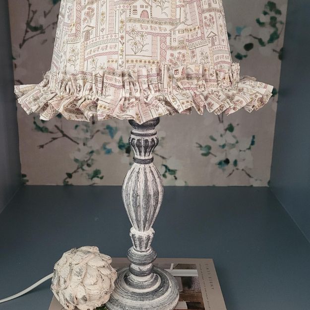 Tapered hand-sewn fabric French drum lampshade featuring alpine flowers and animals in a whimsical design. Finished with ruffle trim for a charming touch, adding a unique and cosy element to any table lamp. Crafted with Liberty London fabric.