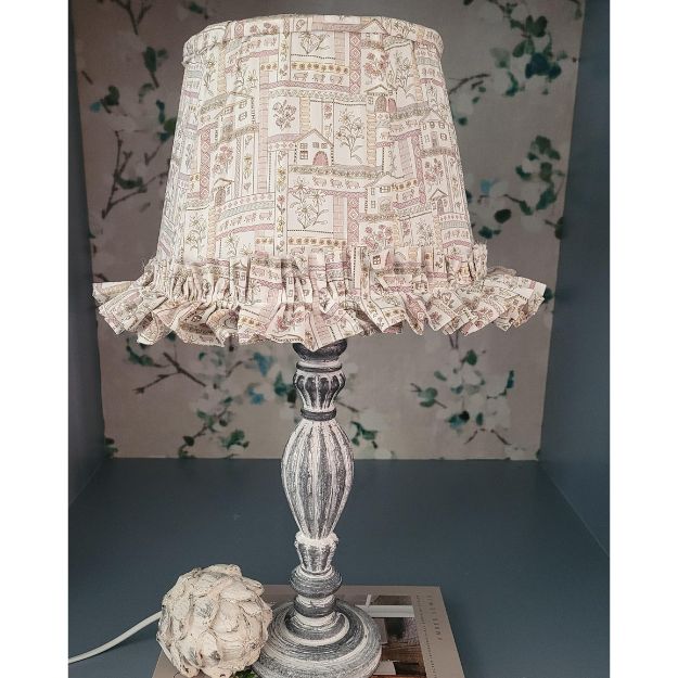 Tapered hand-sewn fabric French drum lampshade featuring alpine flowers and animals in a whimsical design. Finished with ruffle trim for a charming touch, adding a unique and cosy element to any table lamp. Crafted with Liberty London fabric.