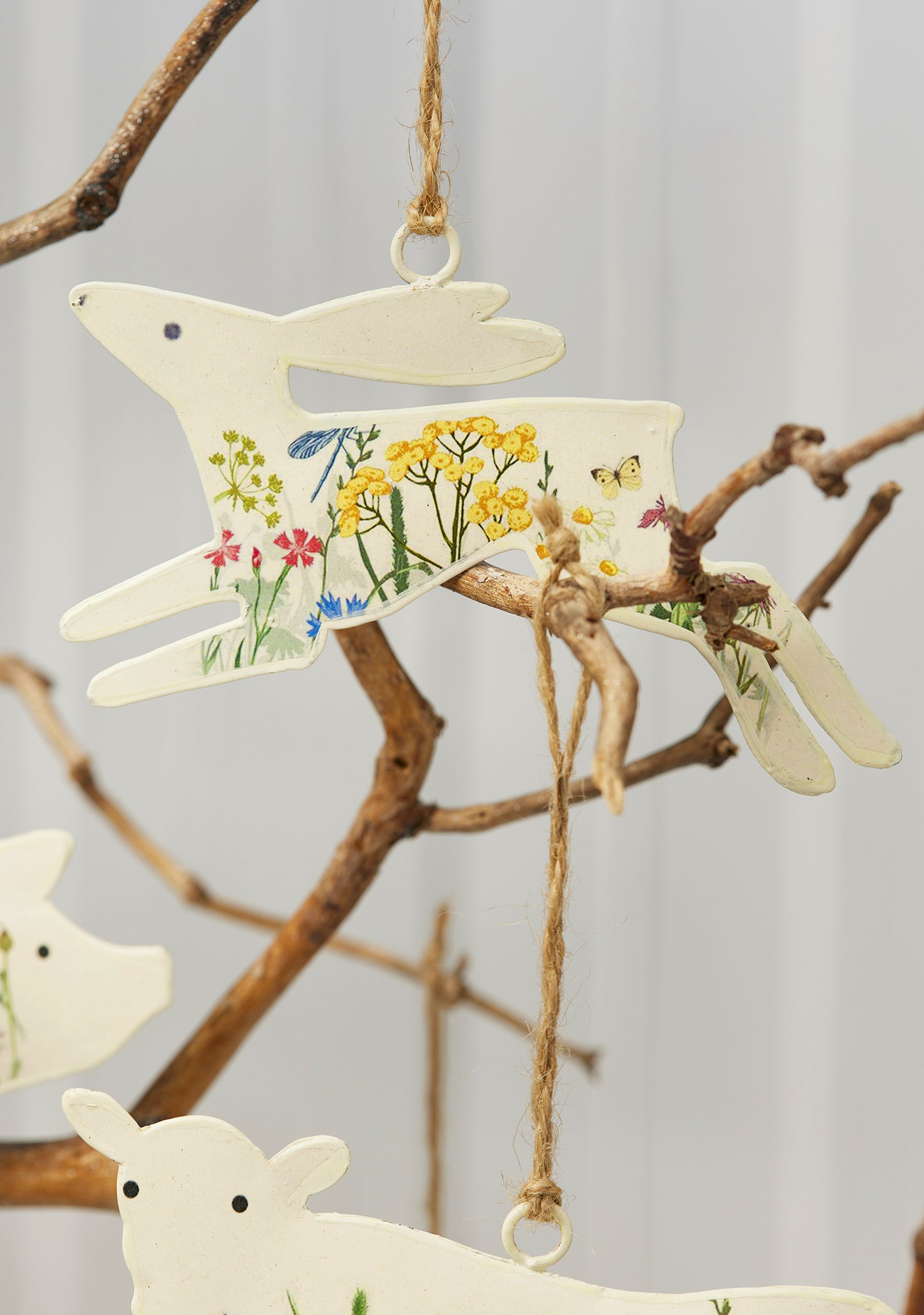 Cream hand-painted metal farm animal decorations — cow, pig, goose, hare and sheep — with floral meadow design and jute hanging string, grouped for display.