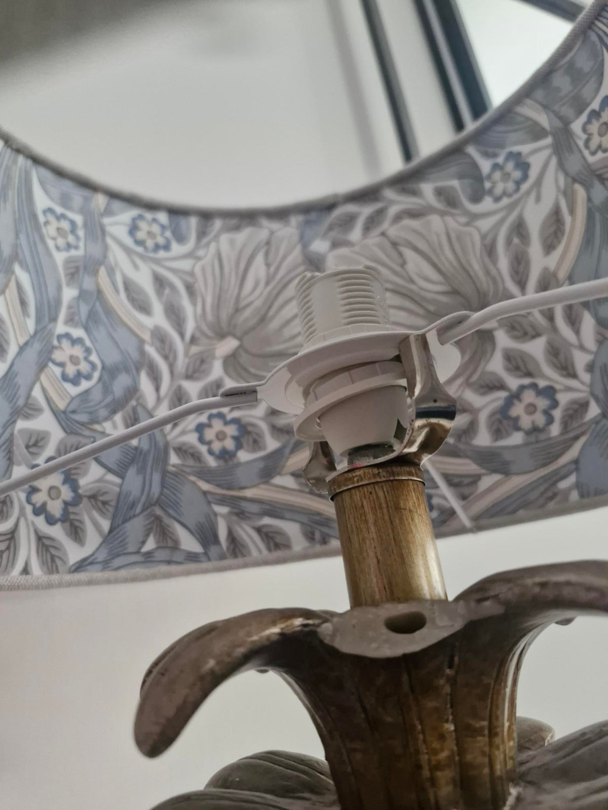 Close-up of a decorative table lamp with a blue and white floral patterned shade, a brass-toned metal stem, and a dark sculptural base.