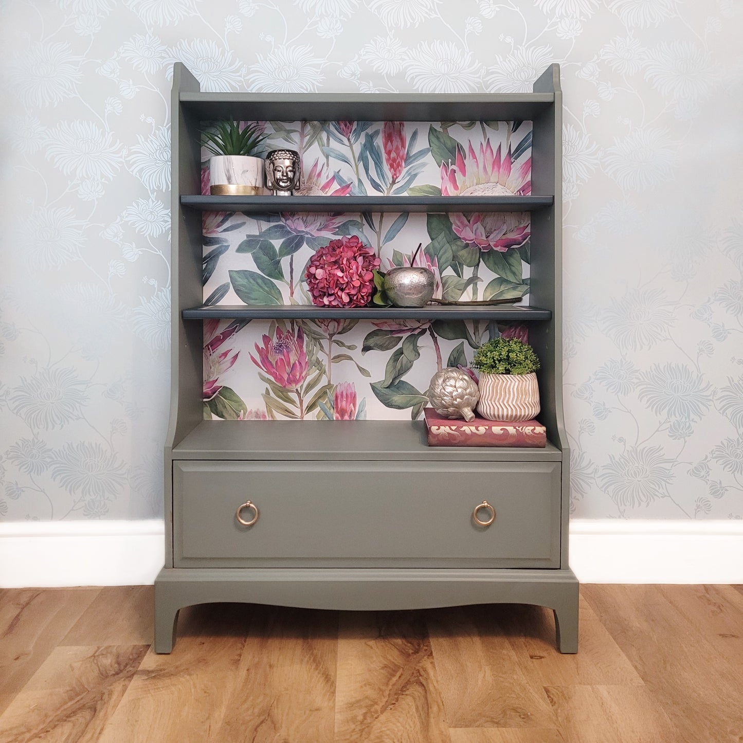 Custom Order - Beautifully upcycled green bookshelf with floral wallpaper backing. The shelves display decorative items and the bottom drawer features elegant gold ring pulls. Perfect for adding a touch of nature-inspired charm to any living room, bedroom, or hallway.