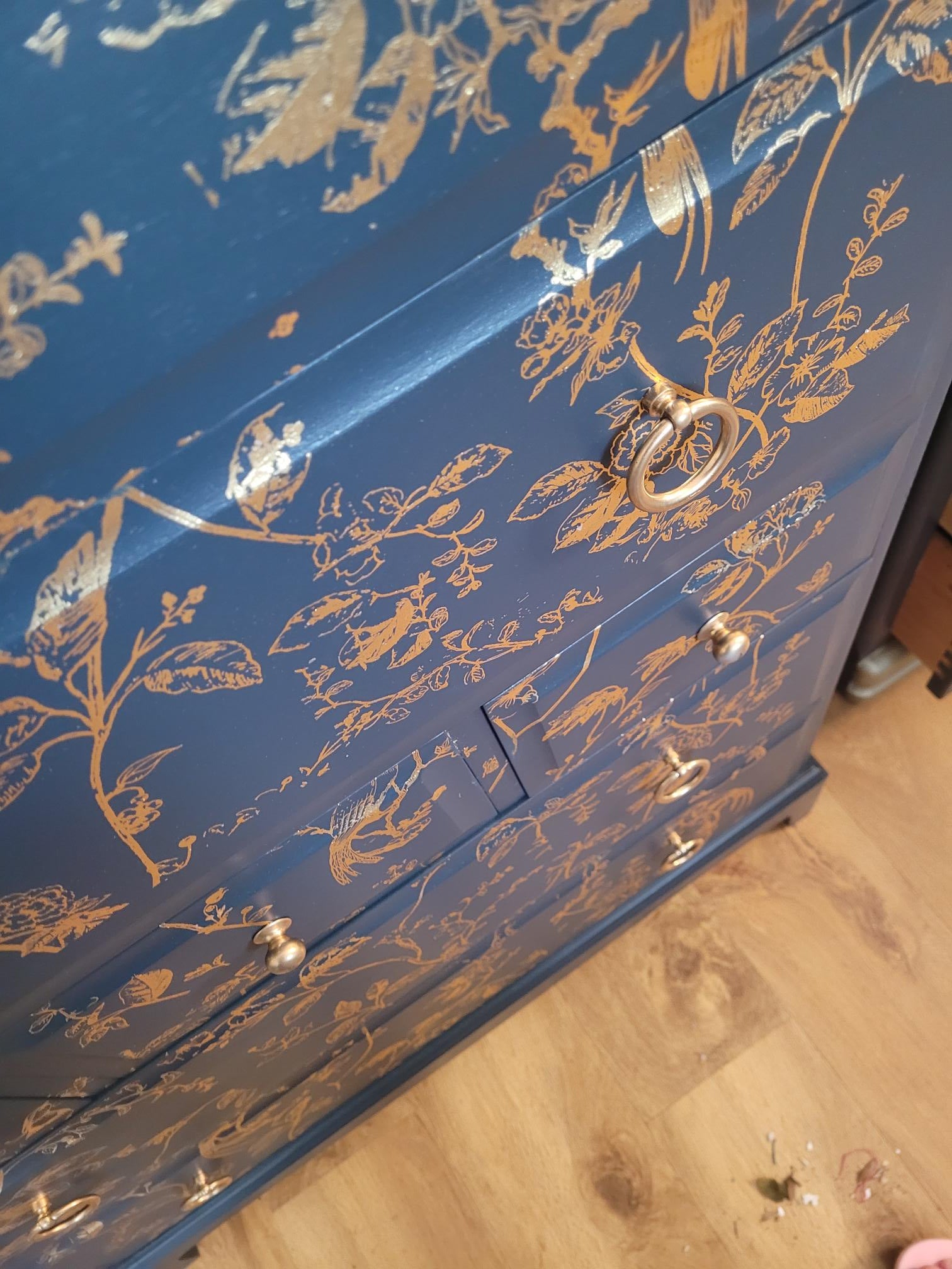 Elegant upcycled navy blue chest of drawers featuring a delicate, hand-painted gold floral design. The drawers are accented with intricate gold knobs, making this piece a sophisticated addition to any living room, bedroom, or hallway.