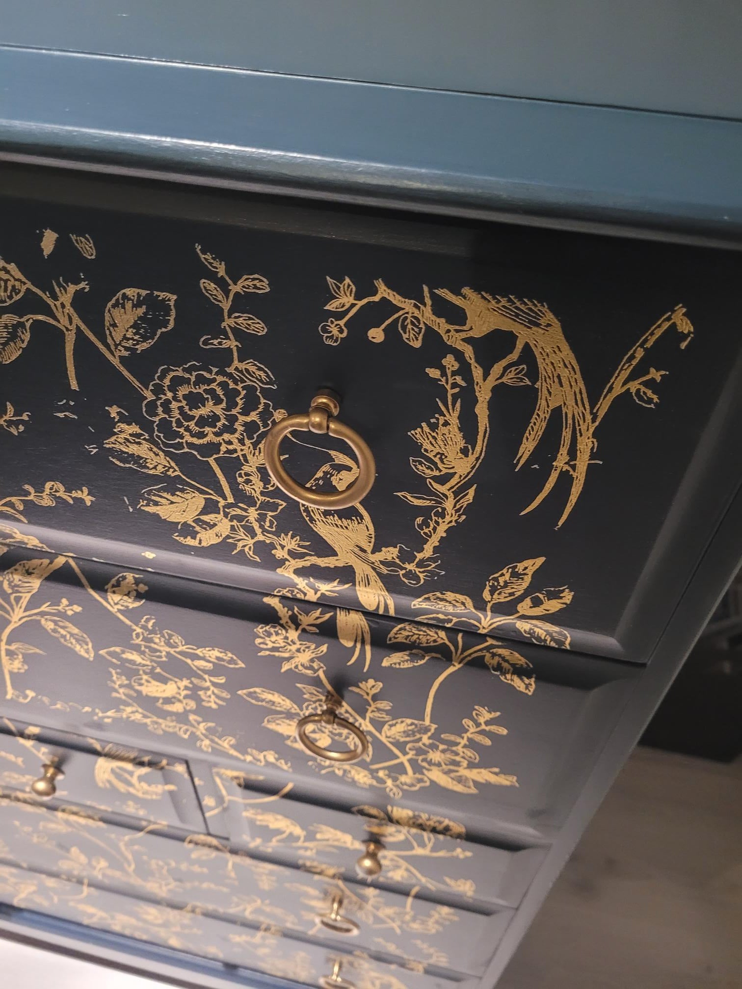 Elegant upcycled navy blue chest of drawers featuring a delicate, hand-painted gold floral design. The drawers are accented with intricate gold knobs, making this piece a sophisticated addition to any living room, bedroom, or hallway.