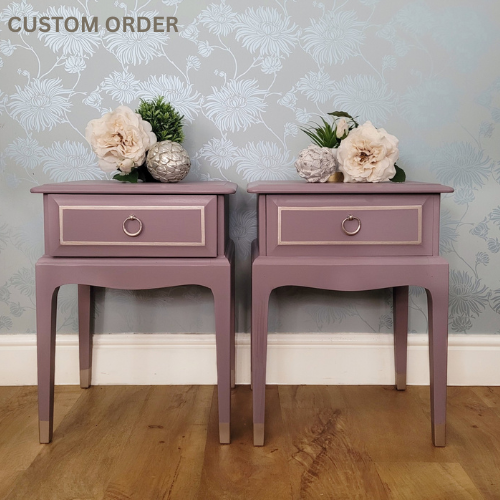 A pair of hand-painted Stag Minstrel bedside tables in Lavender Haze with champagne metallic detailing and lavender toile-lined drawers, styled against a floral wallpaper background.