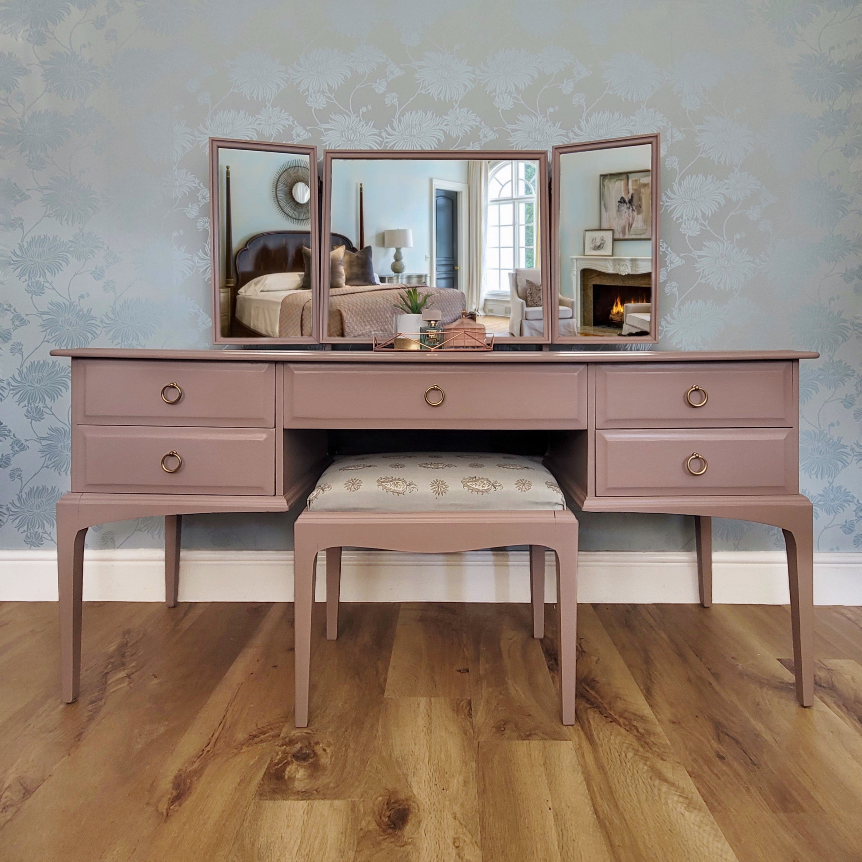 Pink vanity table with mirror and bench in a room with floral wallpaper. Available and in stock for hand painted commission.