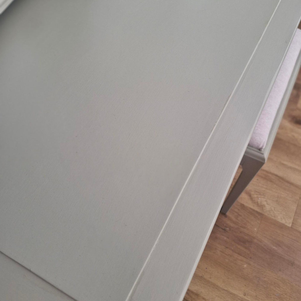 Close-up of a light green wooden table corner with a matching gray chair partially visible, set on a light wood floor.