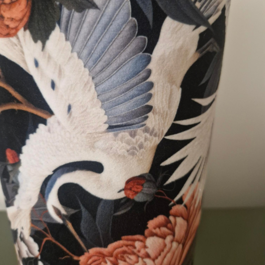 Close-up of a cylindrical product featuring a detailed print of white cranes with blue-gray wings and peach flowers on a black background.