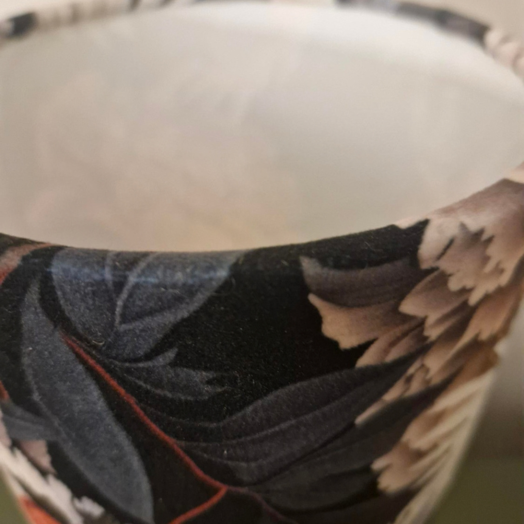 Close-up of a a table lamp rim showing a dark floral pattern with black, gray, and beige tones, with a white interior visible.