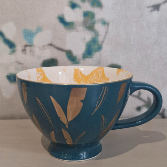Green ceramic cup with orange floral patterns on a neutral background