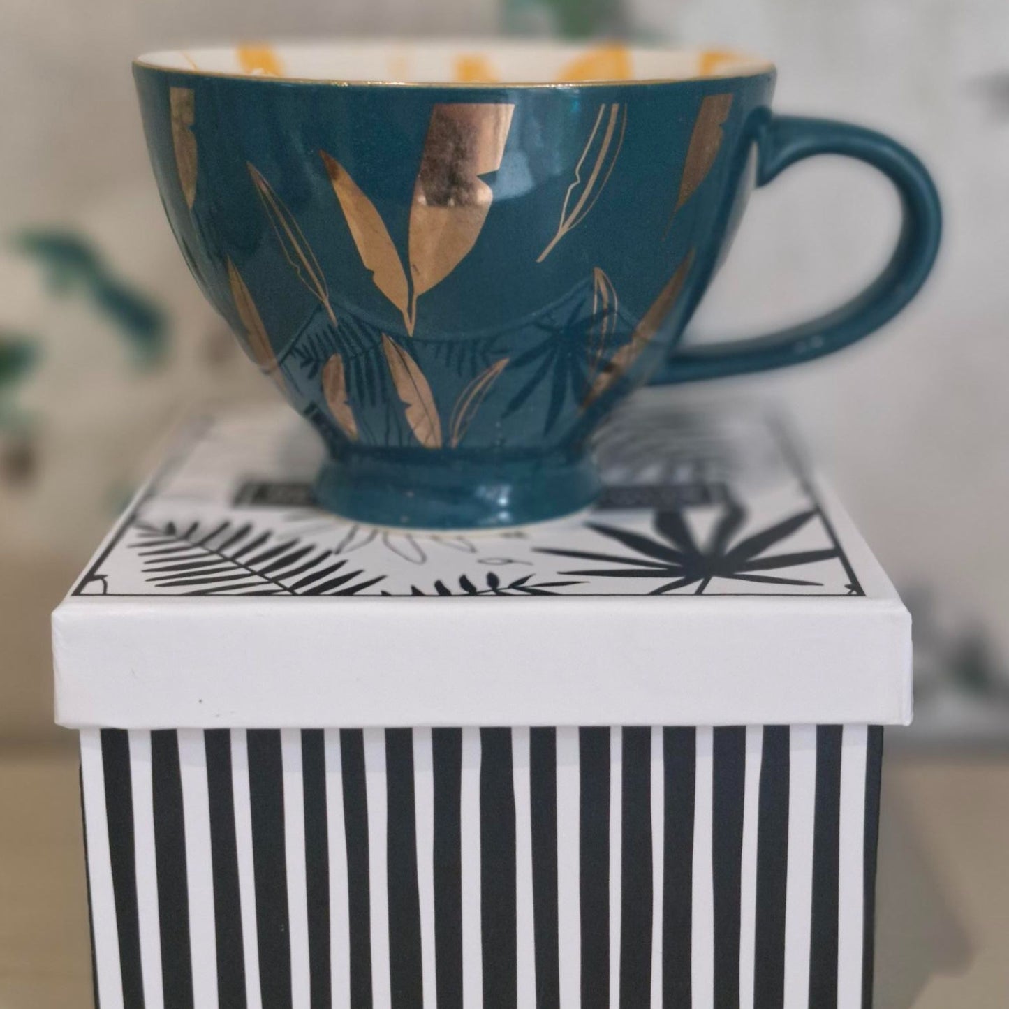 Green / Blue mug with gold leaf design on a white surface with black stripes
