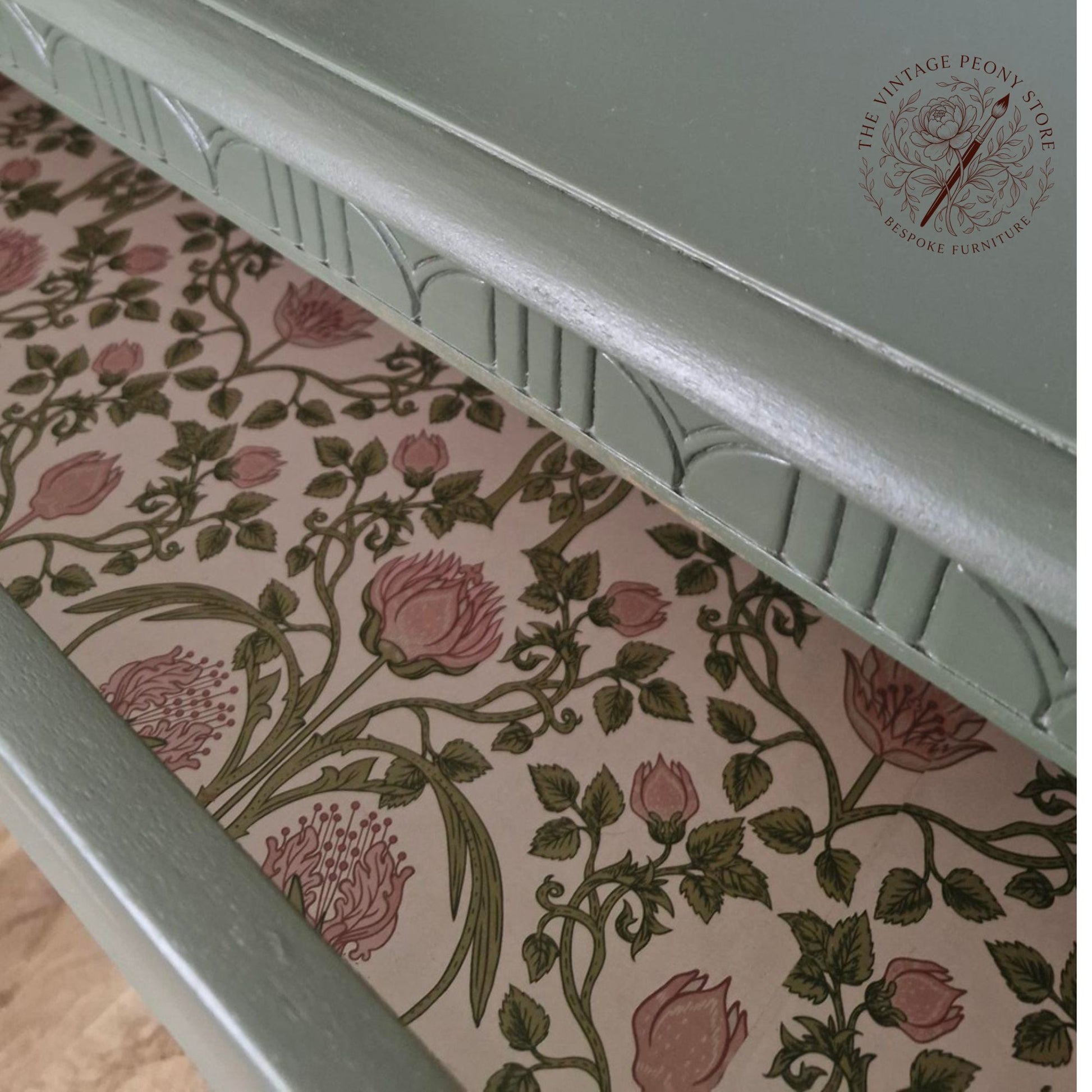 Close-up of the top carved ridge of a Lebus chest of drawers showing a painted finish and a floral lined drawer. 