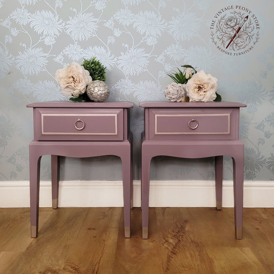A pair of matching dusty mauve side tables with single drawers and circular metal knobs, styled with flowers on top against a floral wallpaper background. A watermark logo for 'The Vintage Peony Store' is visible in the top right corner.