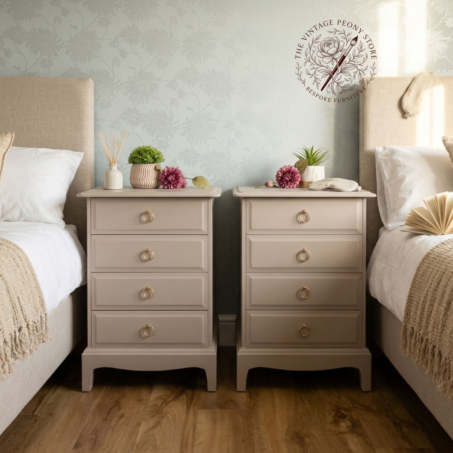 A pair of matching beige nightstands with five drawers and round brass knobs, styled between two beds in a bedroom with a floral wallpaper background.