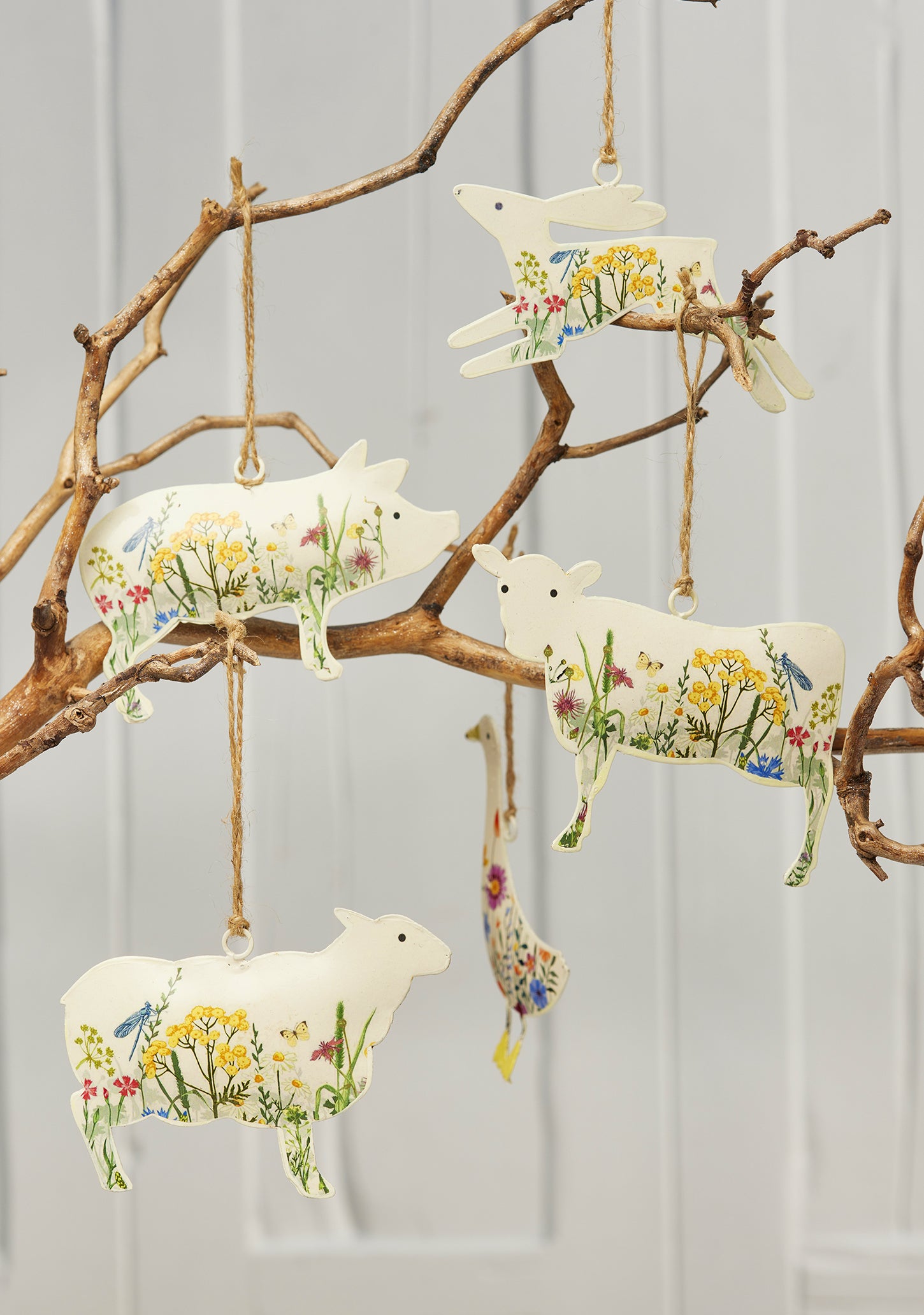 Cream hand-painted metal farm animal decorations — cow, pig, goose, hare and sheep — with floral meadow design and jute hanging string, grouped for display.