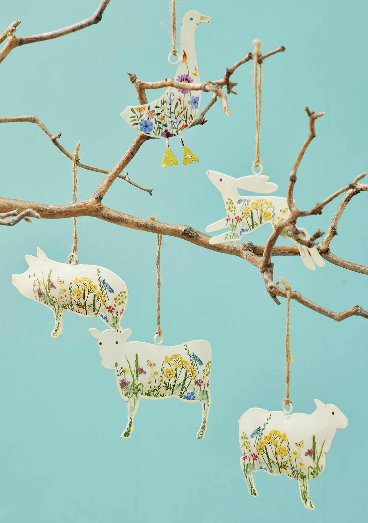 Cream hand-painted metal farm animal decorations — cow, pig, goose, hare and sheep — with floral meadow design and jute hanging string, grouped for display.