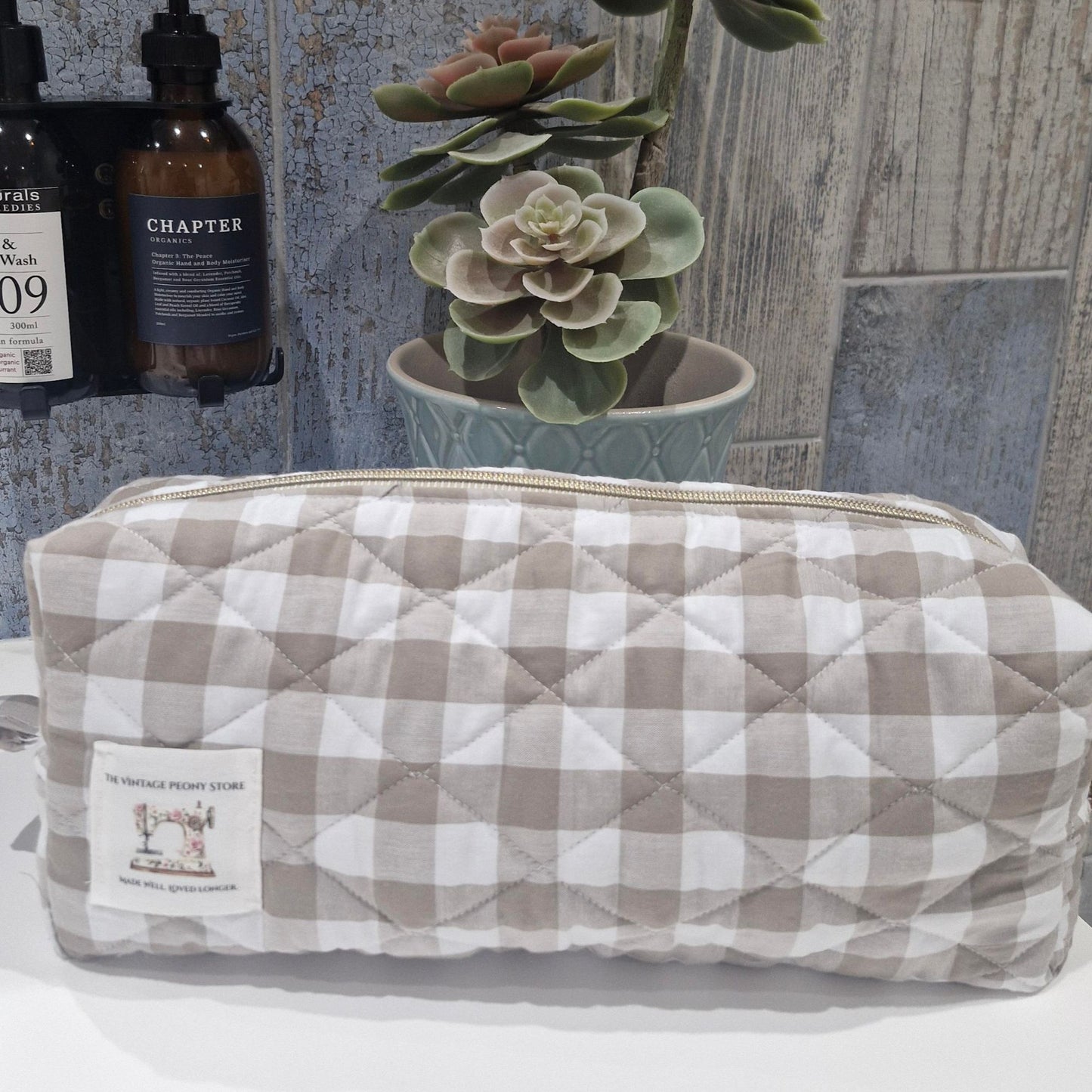Quilted toiletry bag with sand gingham pattern on a surface with decorative items in the background.
