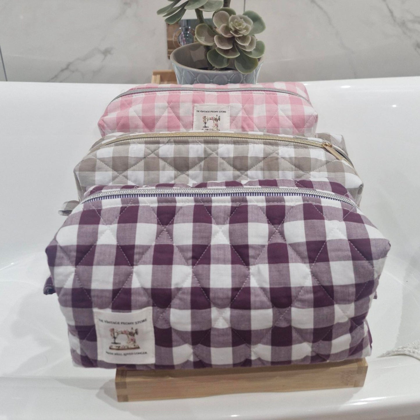 Stack of quilted hair tool bags with pink, sand and plum gingham patterns on a white surface.