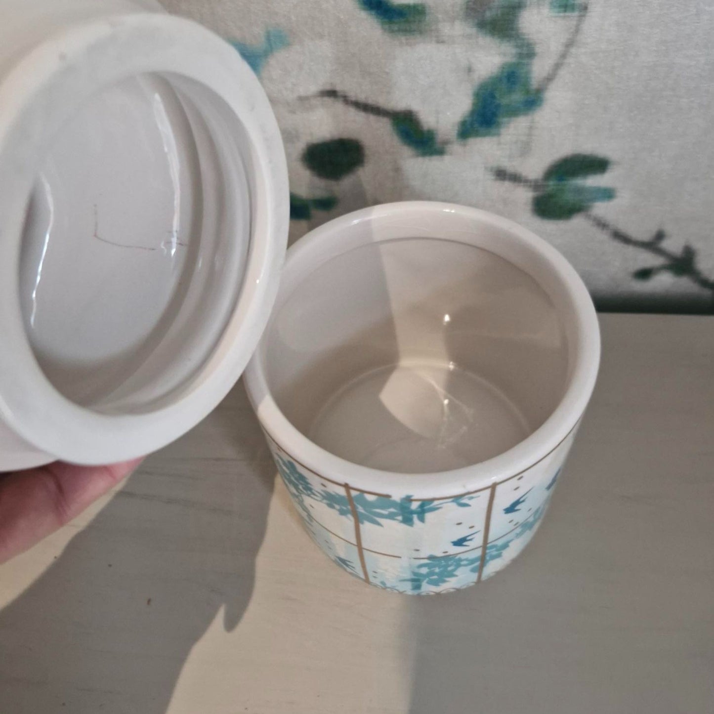 White ceramic lid of peacock storage jar on a floral-patterned surface