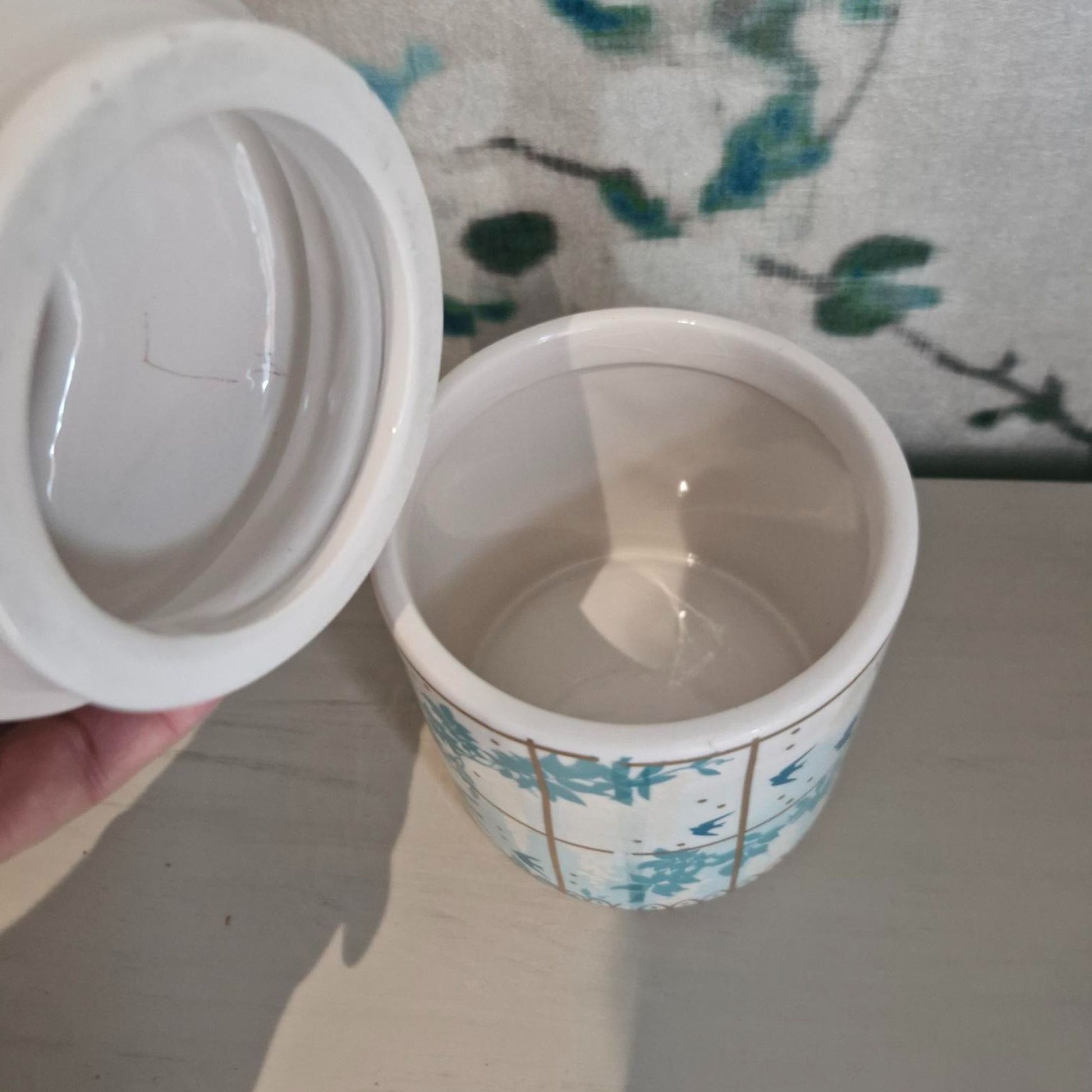 White ceramic lid of peacock storage jar on a floral-patterned surface
