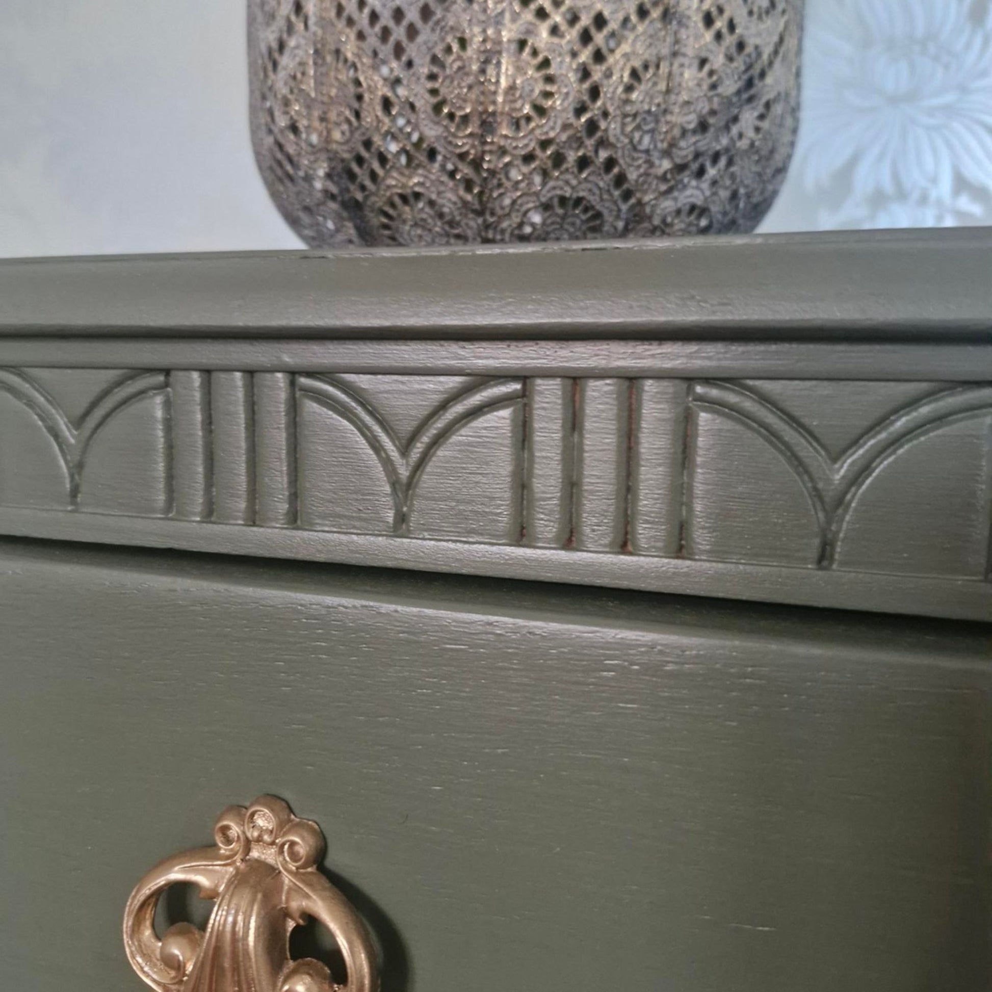 Close-up of a painted Lebus chest of drawers painted inbayberry green, showing carved decorative molding along the top edge and part of a metallic bronze pull handle.