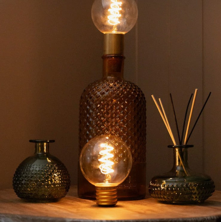 Warm glowing filament LED bulb on wooden surface next to cardboard packaging