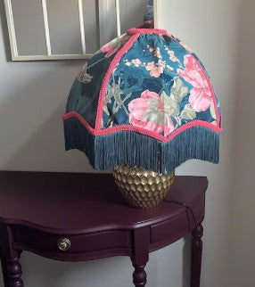 Decorative lamp with floral design on a wooden table against a plain wall.