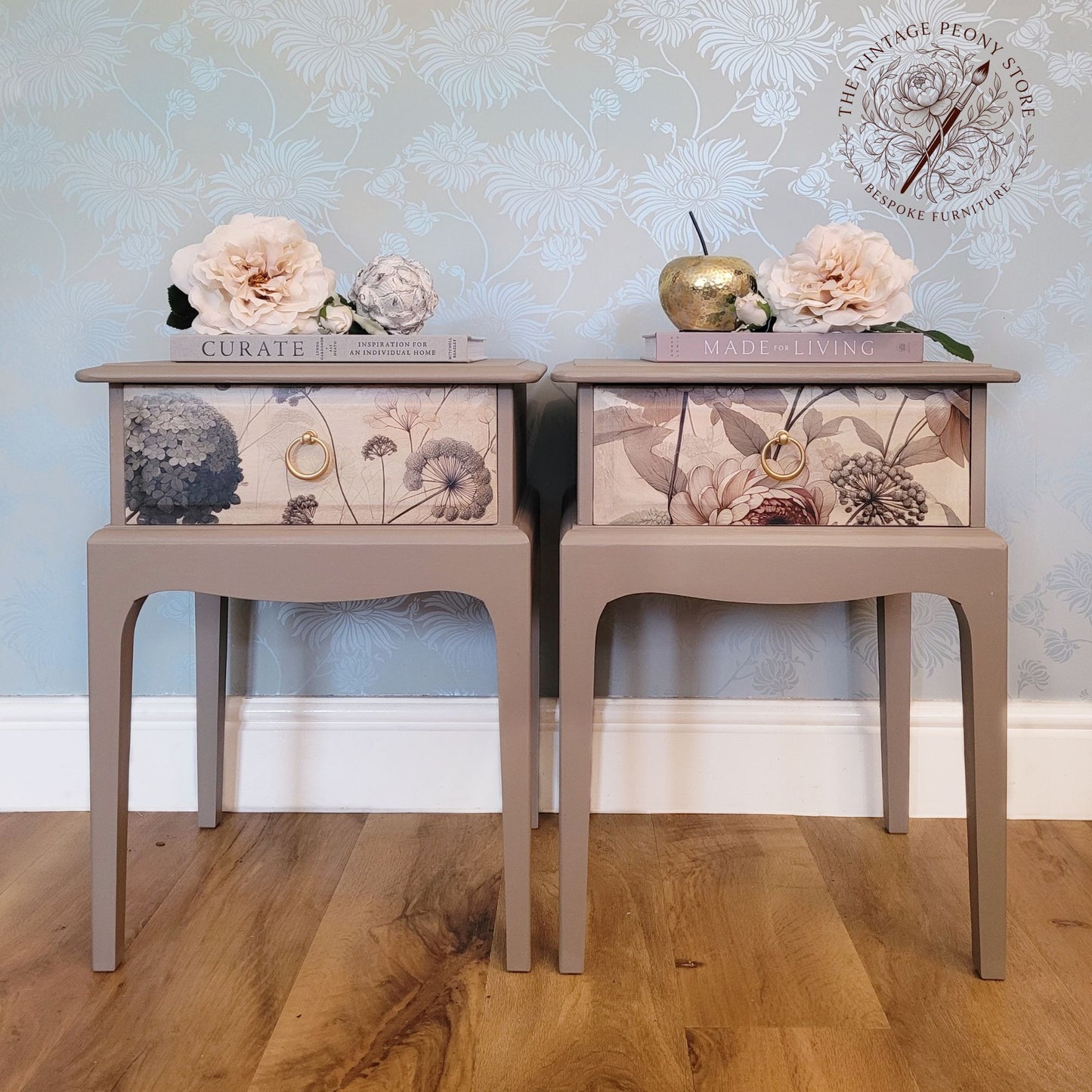Two matching painted side tables with floral drawer fronts, styled with flowers and books against a patterned wallpaper background.