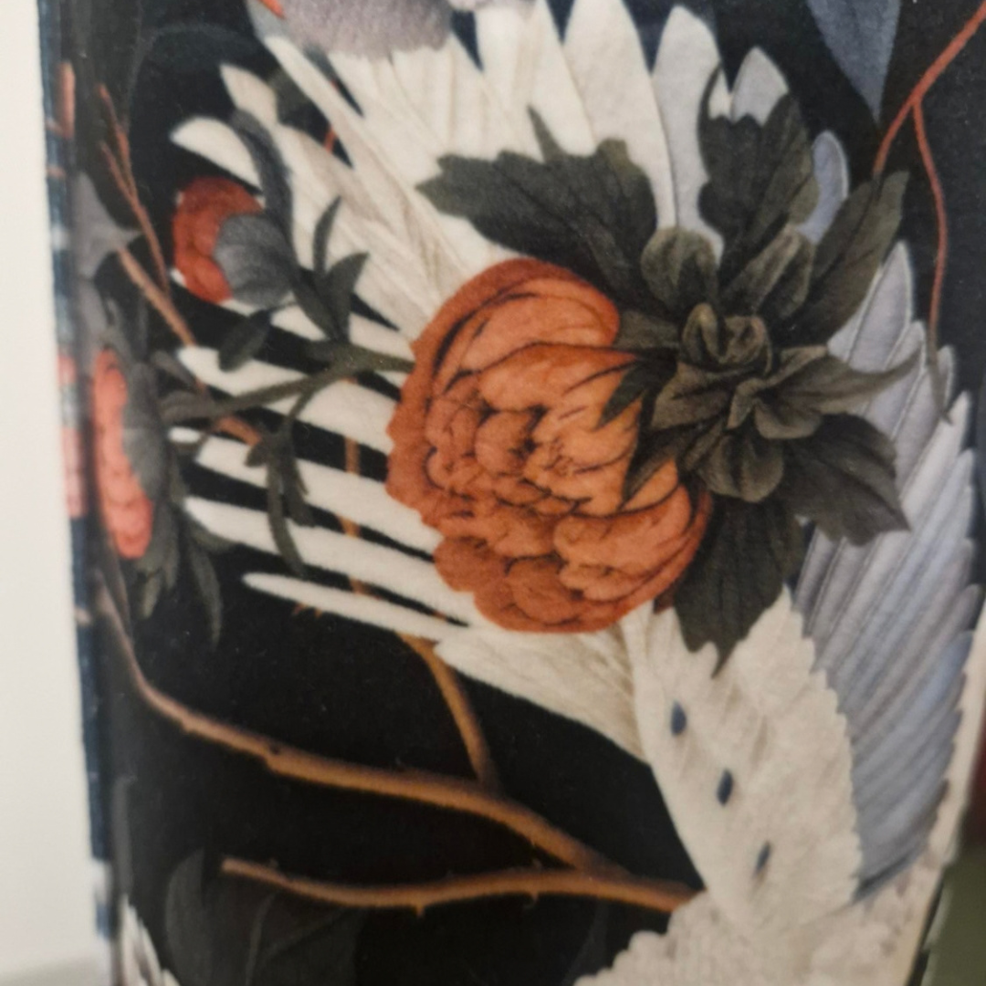 Close-up of a decorative floral and bird pattern on a dark background, featuring white cranes, orange flowers, and dark green leaves.