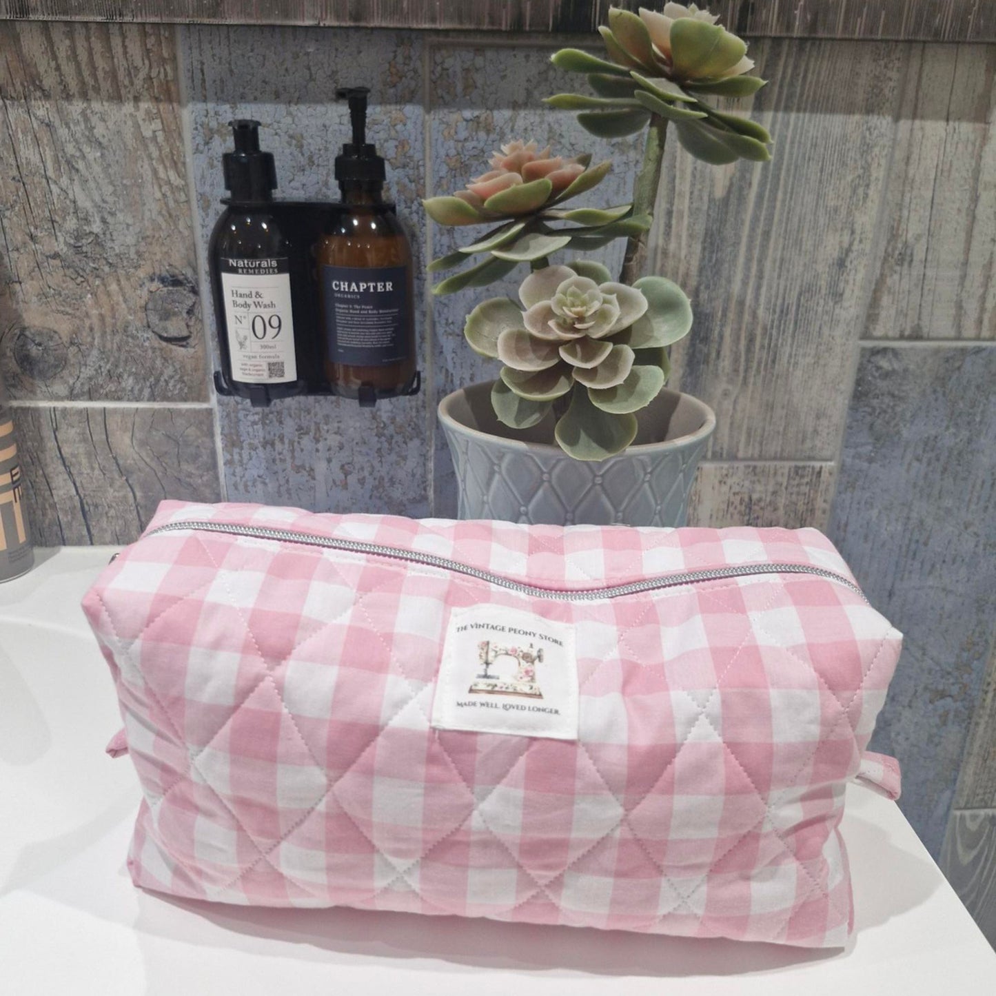 Pink gingham makeup bag with a brand label on a bathroom counter.