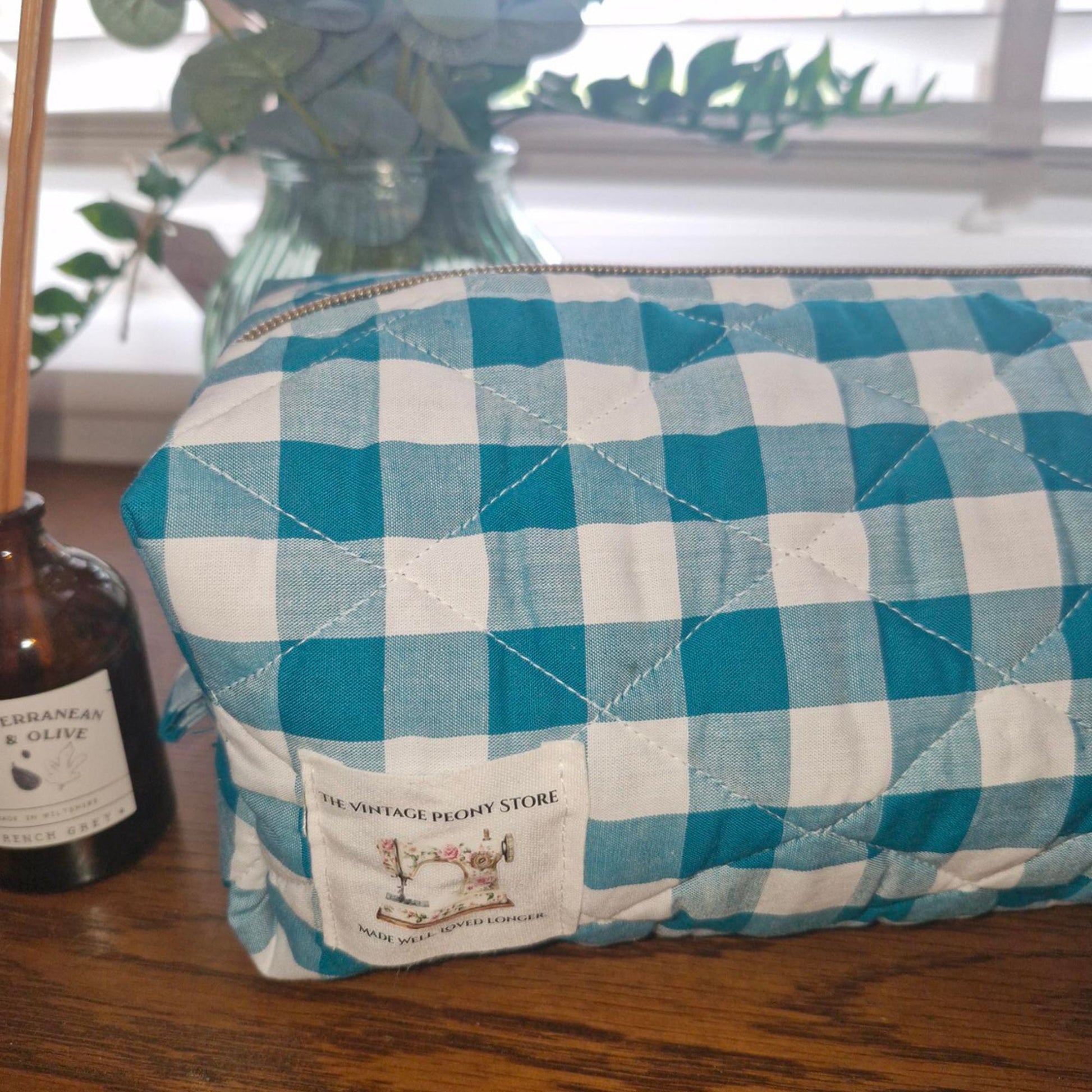 Teal gingham pouch / hair tool bag with a visible brand label on a wooden surface.